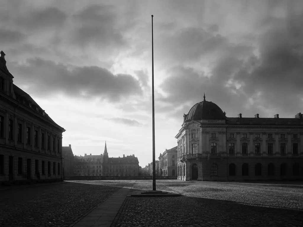 Ett tomt europeiskt torg i svartvitt med långa skuggor, sent 1920-tal